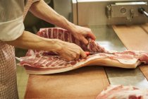 Крупным планом мясника режущие стороны свинины на столе — стоковое фото
