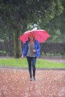 Дівчинка-підліток з червоним парасолька гуляти під дощем — стокове фото
