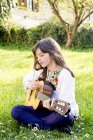 Девушка, сидящая на лугу, играет на гитаре — стоковое фото