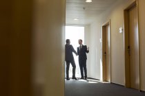 Далекий взгляд бизнесменов в коридоре пожимающих руки — стоковое фото