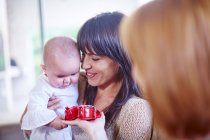 Mutter hält Baby mit Frau, die Babyschuhe präsentiert — Stockfoto