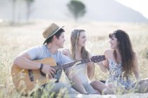 Amis jouant de la guitare assis dans le champ — Photo de stock