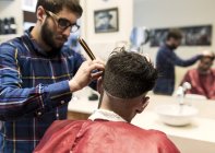 Парикмахер бреет волосы молодого человека в парикмахерской — стоковое фото