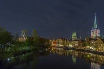 Alemania, Luebeck, paisaje urbano por la noche con el edificio de la iglesia reflexionando sobre la superficie del agua - foto de stock