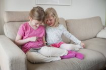 Deux sœurs avec tablette numérique sur canapé — Photo de stock