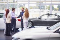 Car dealer meeting with clients in showroom — Stock Photo