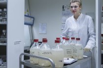 Biologiste en laboratoire poussant chariot avec bouteilles — Photo de stock