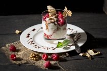 Dessert in glass with raspberries, curd, yoghurt, dried apple, almond slivers and chocolate sauce — Stock Photo