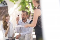 Cameriera con vassoio e coppia seduta all'aperto degustazione vino rosso — Foto stock
