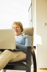 Mujer mayor en casa usando portátil - foto de stock