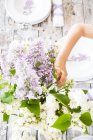 Mädchen bastelt Strauß mit Fliederblumen auf Holzdecktisch — Stockfoto