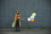Young woman with suitcase holding bunch of balloons — Stock Photo