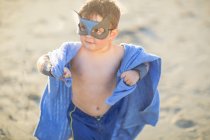 Kleiner Junge am Strand verkleidet als Superheld mit Maske und Handtuch — Stockfoto