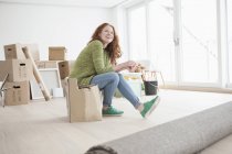 Молодая женщина в новой квартире сидит на картонной коробке — стоковое фото