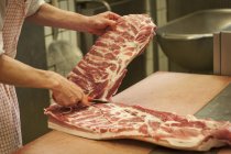 Крупным планом мясника режущие стороны свинины на столе — стоковое фото