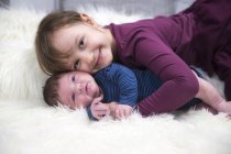 Sorridente bambina con neonato fratello su pelle di pecora — Foto stock