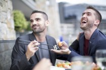 Пара геев, поедающих суши в ресторане на открытом воздухе — стоковое фото