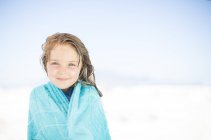 Smiling girl on beach wrapped in a towel — Stock Photo