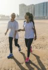 Две спортивные девушки с наушниками идут по пляжу — стоковое фото