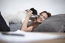 Jeune femme jouant avec le chien sur le canapé — Photo de stock