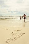 Two young boys at beach running into seawater, word Ferien written in sand — Stock Photo