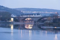 Alemanha, fronteira com o Luxemburgo, Wasserbillig, ponte sobre a água e edifícios na costa à noite — Fotografia de Stock