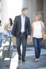 Бізнесмен тягне валізу і ходить біля жінки — стокове фото