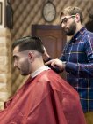 Парикмахер стрижет волосы молодого человека в парикмахерской — стоковое фото