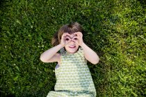 Kleines Mädchen liegt auf einer Wiese und schaut durch ihre Finger — Stockfoto
