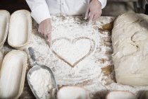 Hembra panadero dibujo corazón en harina en una mesa de madera - foto de stock