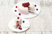 Raspberry cream cake with piece on plate on patterned fabric — Stock Photo