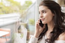 Smiling young woman on cell phone looking out of window — Stock Photo