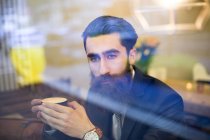 Fashionable man with beard sitting in coffee shop, drinking coffee — Stock Photo