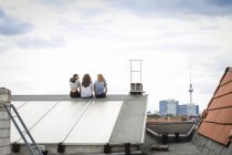 Германия, Берлин, вид сзади на трех друзей, сидящих бок о бок на крыше — стоковое фото
