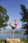 Молодая женщина делает упражнения на камне, берегу озера — стоковое фото