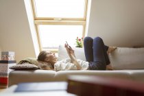 Расслабленная женщина лежит на диване с помощью мобильного телефона — стоковое фото
