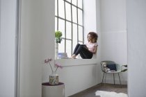 Жінка, сидячи на підвіконні, використовуючи цифровий планшетний — стокове фото