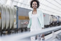 Portrait of smiling young woman with earphones and smartphone at platform — Stock Photo