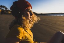 Ragazza adolescente che indossa berretto e cuffie seduto sulla spiaggia — Foto stock