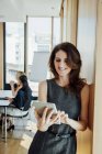Femme d'affaires souriante au bureau en utilisant une tablette numérique avec une réunion en arrière-plan — Photo de stock