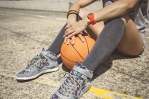 Молодая женщина, сидящая на площадке для бакетбола с мячом между ног — стоковое фото