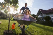 Father with daughter in wheelbarrow planting tree in garden — Stock Photo