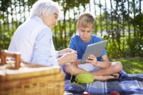 Enkel mit digitalem Tablet und Großmutter auf Picknickdecke — Stockfoto