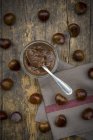 Glass of sweet chestnut cream and sweet chestnuts on kitchen towel and dark wood — Stock Photo