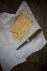 Piece of Asiago stagionato and a pocket knife on parchment paper and dark wood — Stock Photo