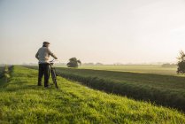 Homem sênior na paisagem rural empurrando bicicleta — Fotografia de Stock