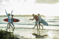 Donna e tre adolescenti con tavole da surf che corrono sul lungomare del mare — Foto stock