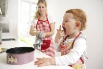 Madre e hija pequeña horneando pastel juntos en su cocina - foto de stock