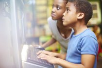 Jovem mulher e menino usando o computador na biblioteca — Fotografia de Stock