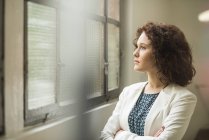 Young businesswoman looking out of window in office — Stock Photo